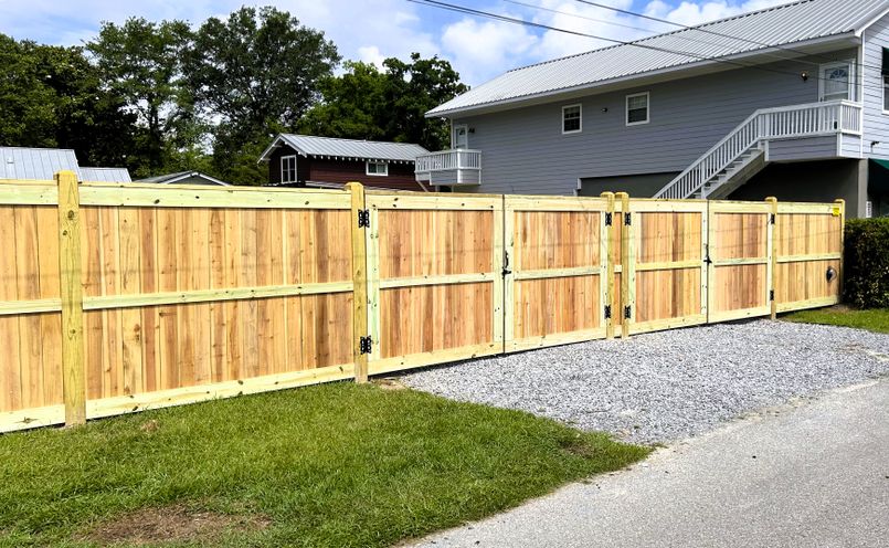 A tall board privacy fence with a framed gate beside a gravel drive