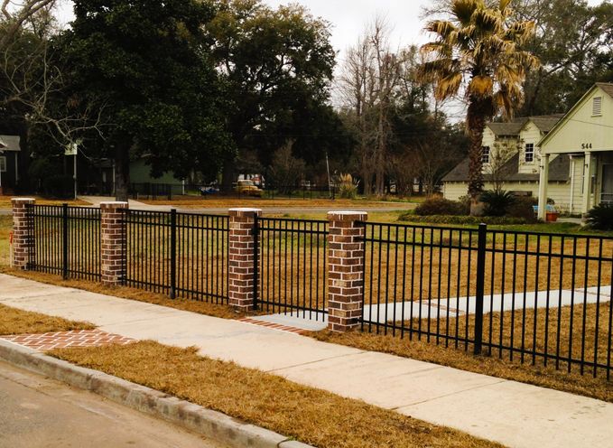 A black metal fence set between brick columns along a sidewalk