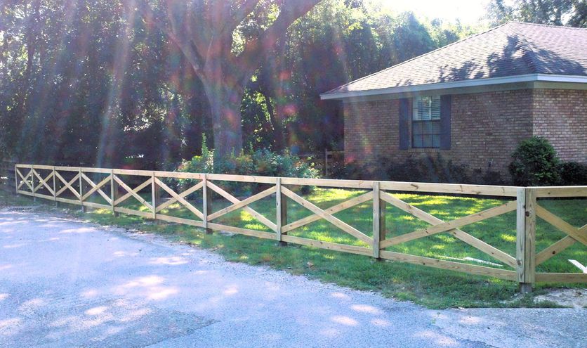 A wood cross-buck ranch fence lining a driveway in front of a brick home