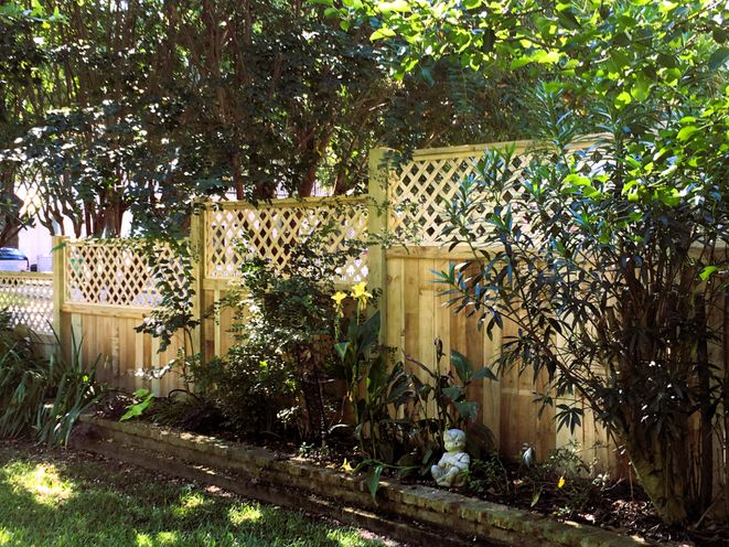 A tall wood privacy fence with a decorative lattice top behind landscaping