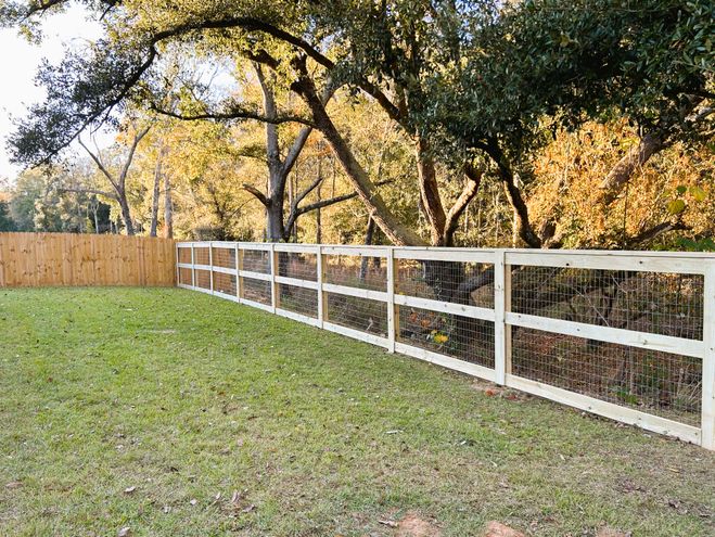 A white three-rail field fence with wire backing along a green pasture