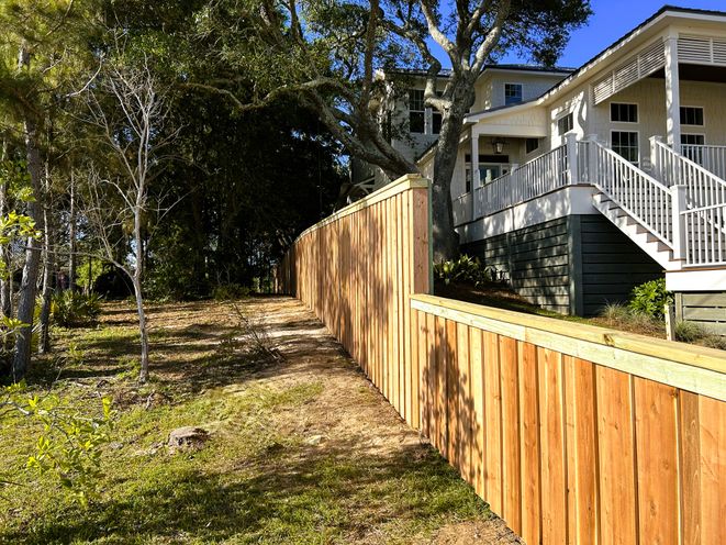 A long cedar privacy fence running downhill alongside a raised house